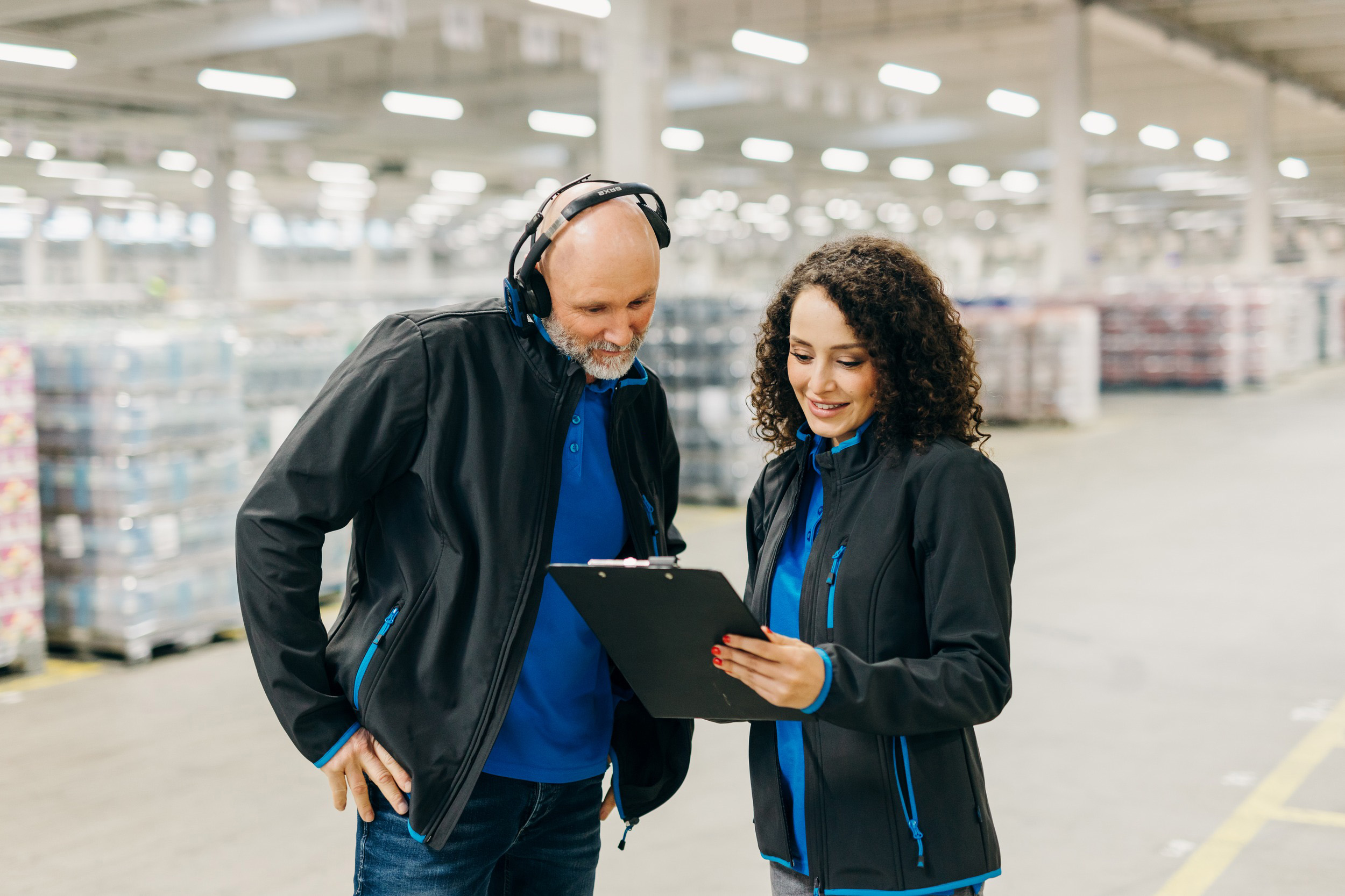 Modernes Business-Foto im Arbeitsumfeld: Mitarbeiter in Corporate-Workwear besprechen Arbeitsprozesse in einer hellen Industriehalle